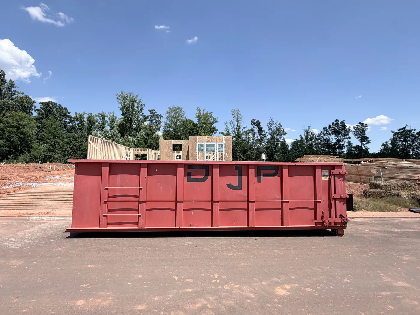 Side view of a DJP 30-yard roll-off dumpster on a new-construction lot, framing lumber behind it