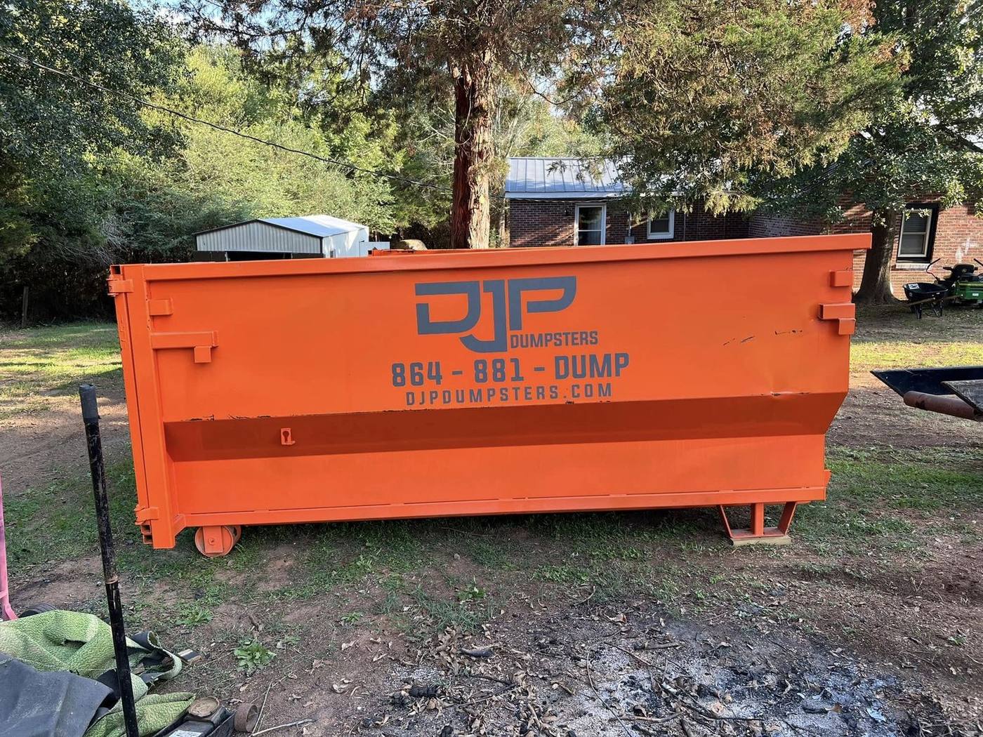 An orange DJP dumpster on the lawn of a brick ranch house