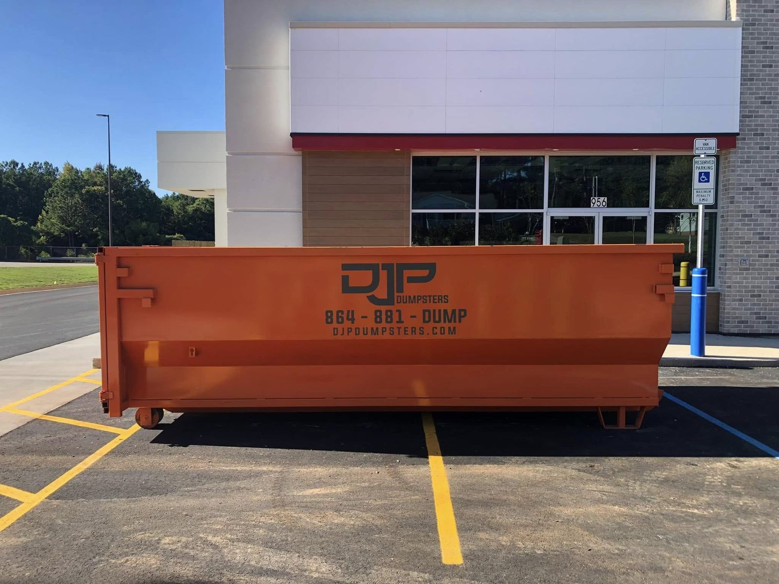 An orange DJP dumpster in the parking lot of a commercial building