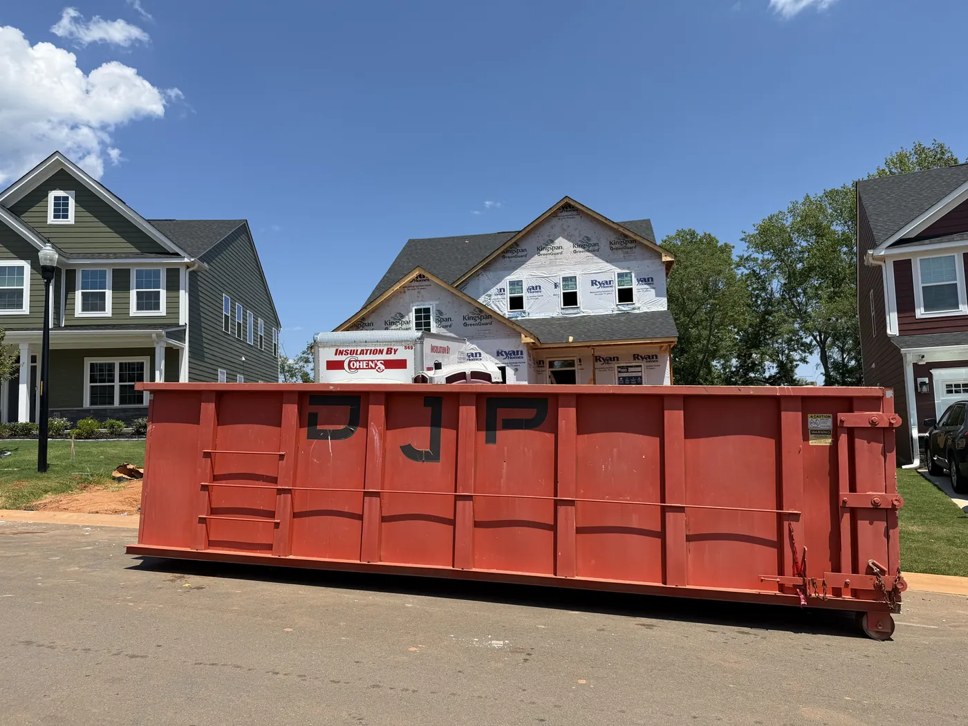 A DJP roll-off dumpster on the street of a neighborhood under construction