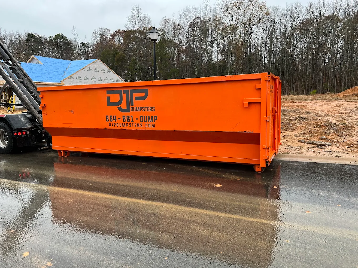 An orange DJP dumpster on a street in front of a house under construction