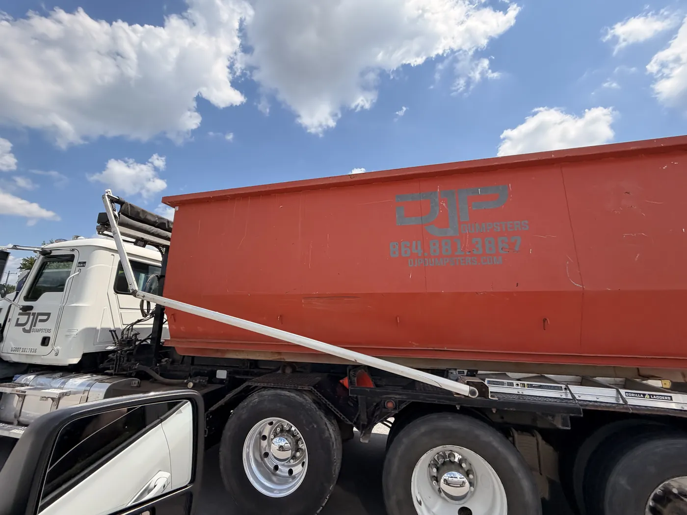 Close-up of a DJP dumpster showing the company name, phone number and website painted on the side