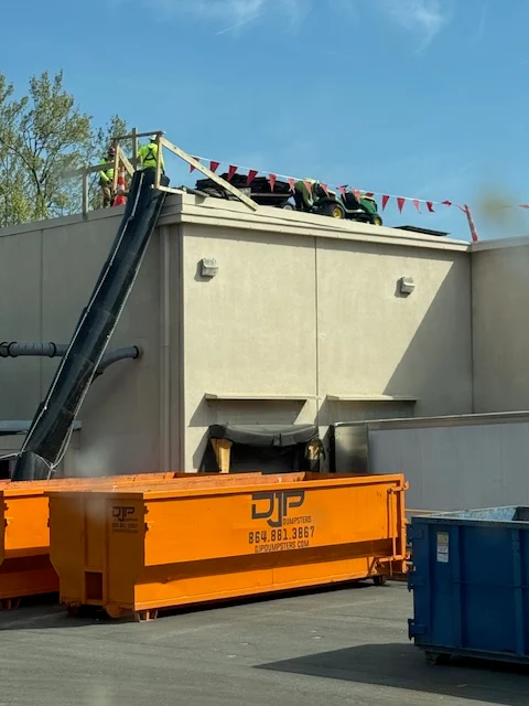 A roofing crew feeding tear-off debris down a chute into a DJP dumpster