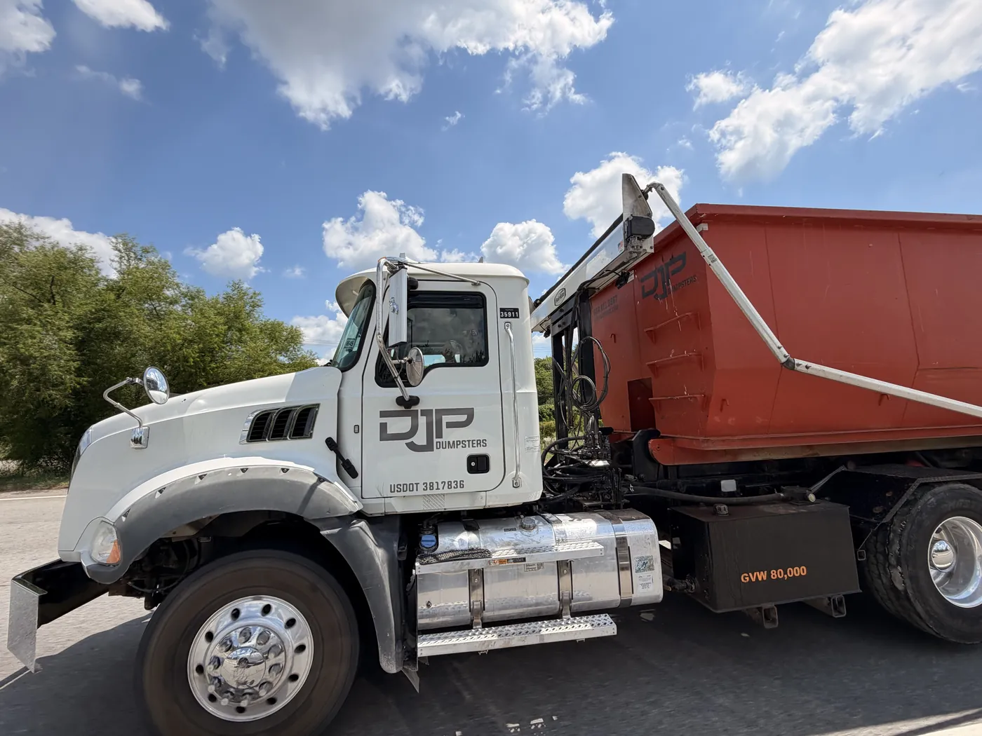 The DJP Dumpsters roll-off truck with the company name on the door and a loaded dumpster on the back