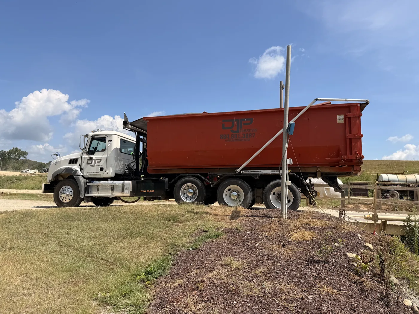 A DJP roll-off truck carrying a loaded orange dumpster out to the tipping site