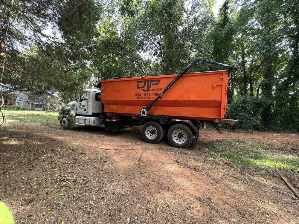 A DJP roll-off truck setting an orange dumpster with the hook arm extended